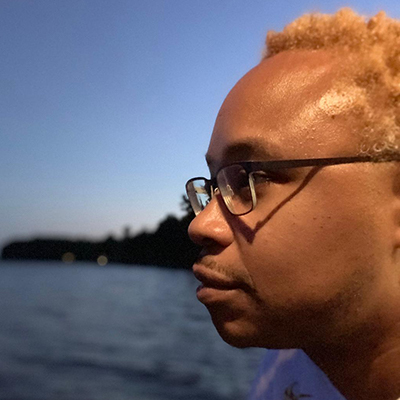 Picture of the artist Deon Best wearing glasses and looking over a lake